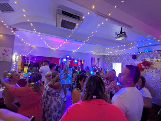 Party-goers dancing under warm and purple party lights with string lights across the ceiling.